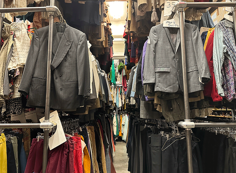 Alt: A photo shows a three racks of clothing, stacked one on top of another, inside a large storage room.