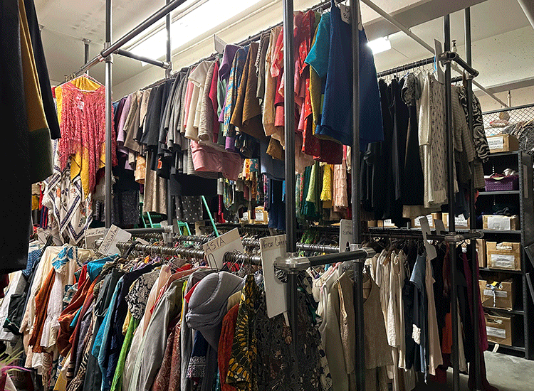 A photo shows multiple racks of clothing, stacked one on top of another, inside a large storage room.