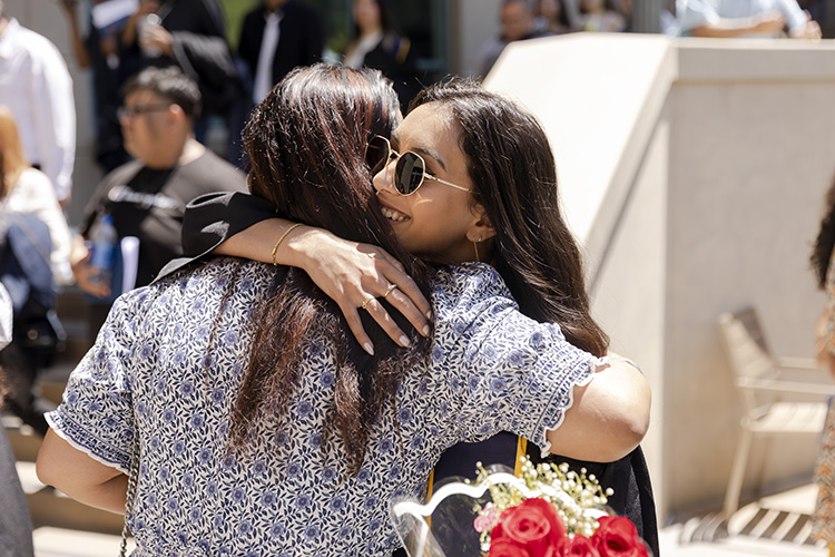 A graduate wearing sunglasses hugs another person