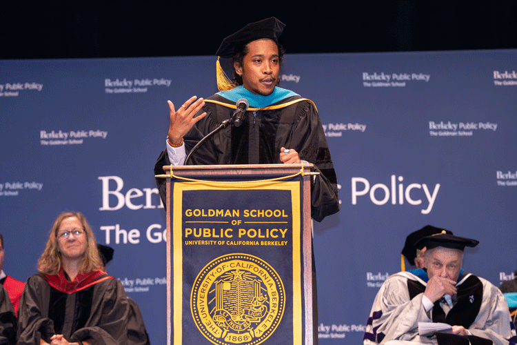 Tennessee state Rep. Justin Jones, in graduation attire, stands behind a lectern and gestures as he speaks to graduating students at the Goldman School of Public Policy