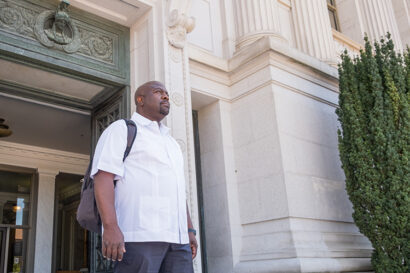 man in white shirt walking out of building looking into distance