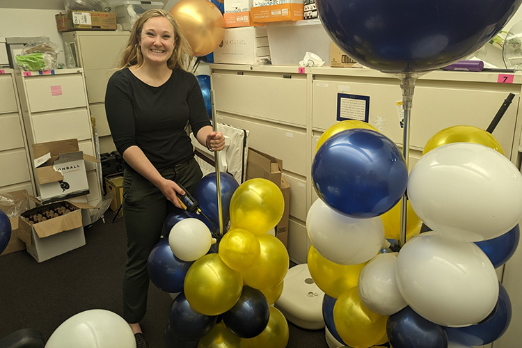 A staff member at the business school pumps up reusable vinyl blue, gold and white balloons for an event. The school has banned single-use balloons.