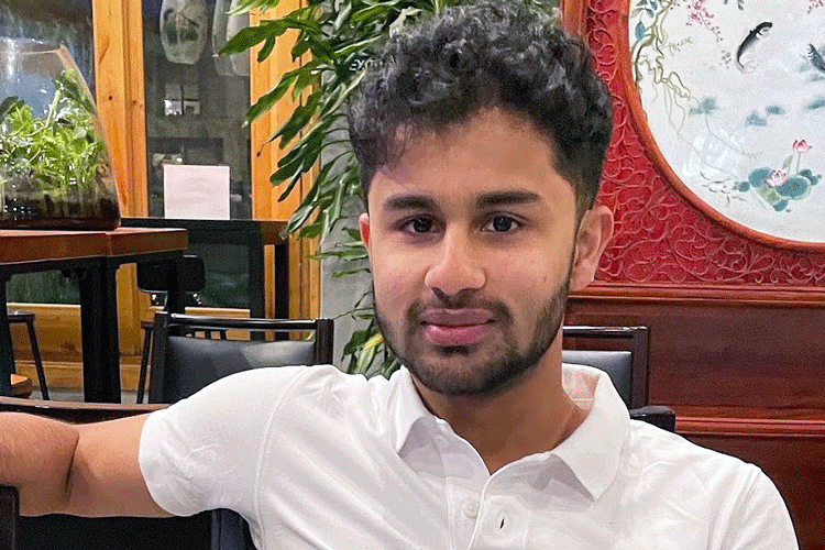 informal portrait of Rohith Sajith in a white polo shirt, sitting down, right arm extended, with Asian art and a terrarium in the background