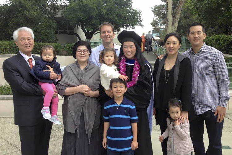 sunny lee, in a cap and gown, stands next to many generations of family and smiles