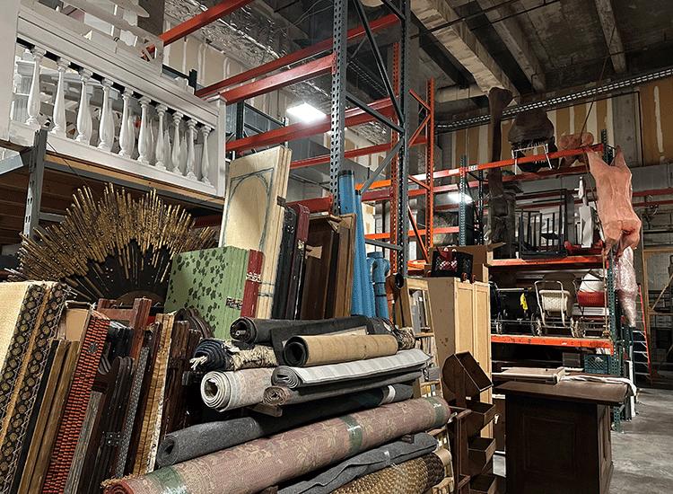 A large, two-story storage room contains racks filled with rugs, old furniture and other random items.