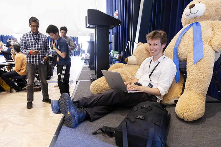 A hacker sitting on stage with a big teddy bear.