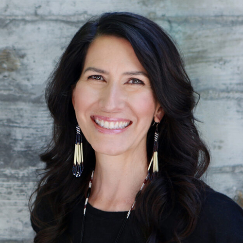 headshot of a person with long, dark hair and beaded earrings smiling widely