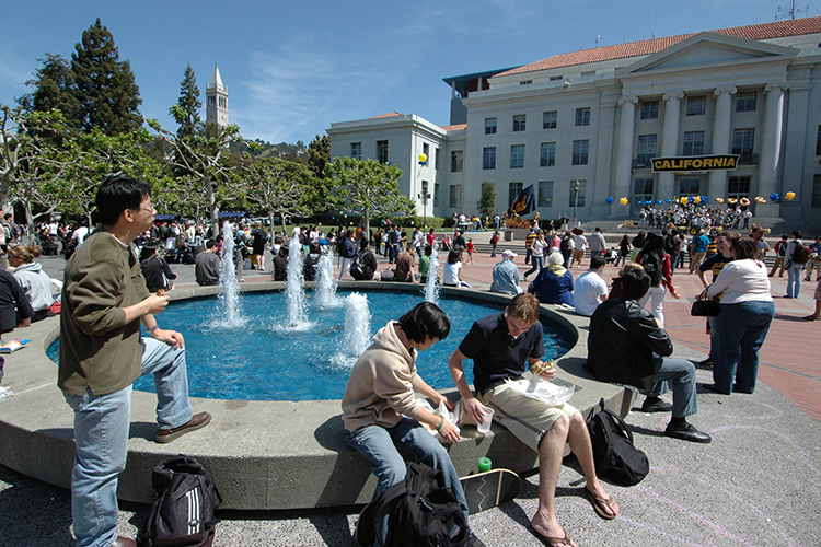 Students sit on the edge of Ludwig's Fountain on Sproul Plaza on a sunny day.