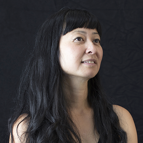 headshot of a person with really long dark hair smiles slightly, looking across the frame