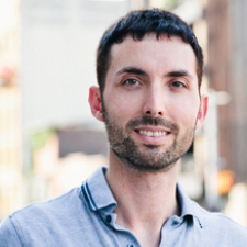 headshot of a person with short, dark hair wearing a collared shirt standing outside and smiling