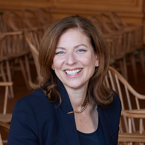 headshot of a person with shoulder-length auburn hair sitting on a chair inside and smiling widely