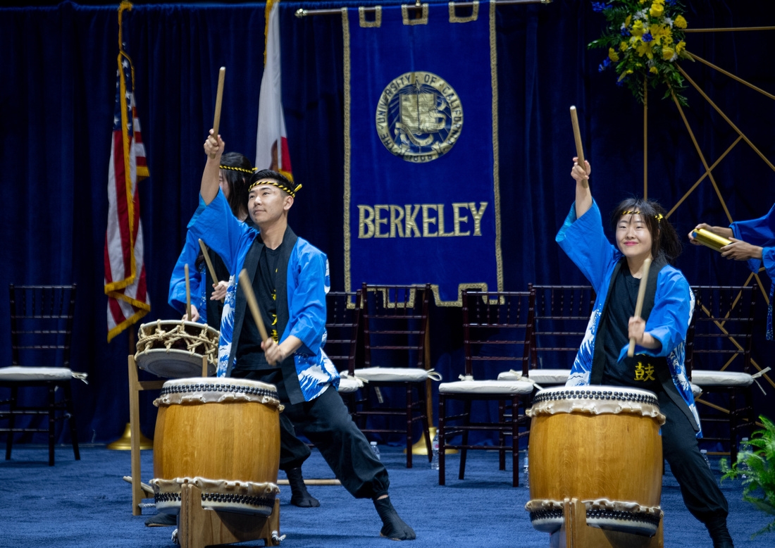 two people with the arms raised play large drums