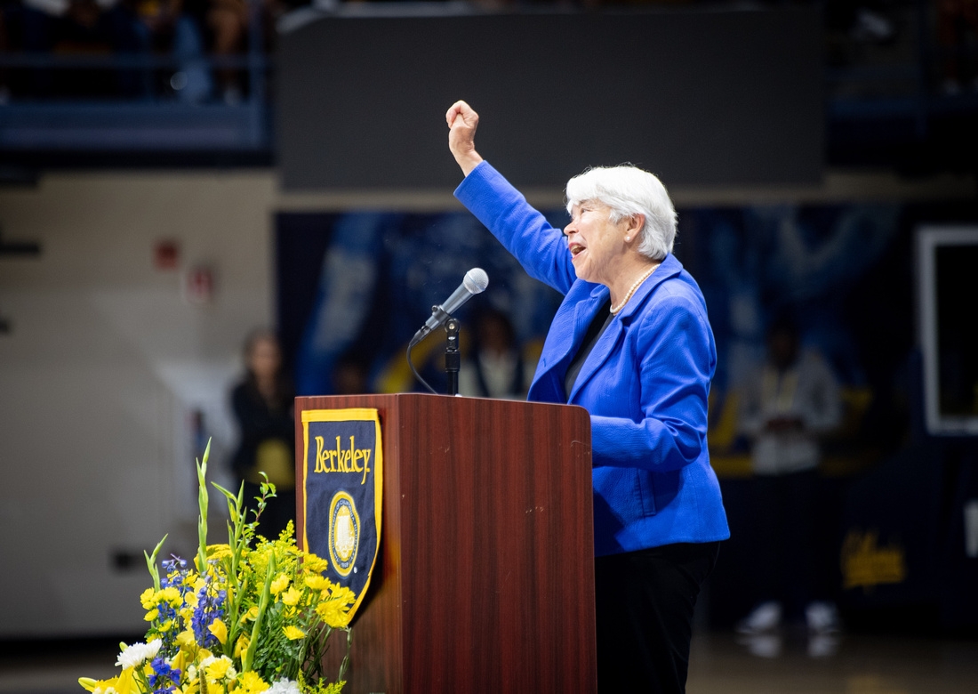 a woman in a blue blazer at a podium raises an arm and cheers