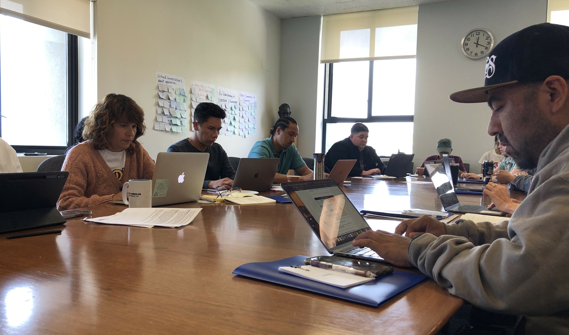 Teachers sit at a conference table using their laptops intently.