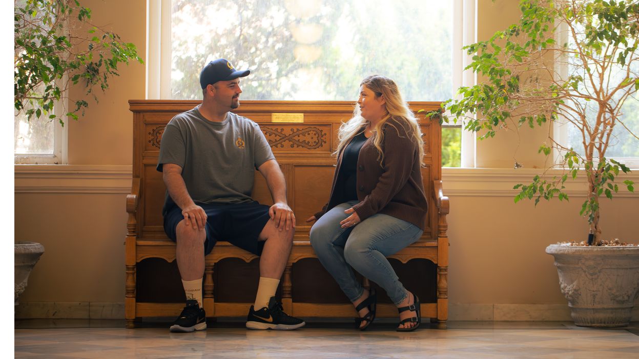 two people sit on a bench talking in front of a brightly lit window