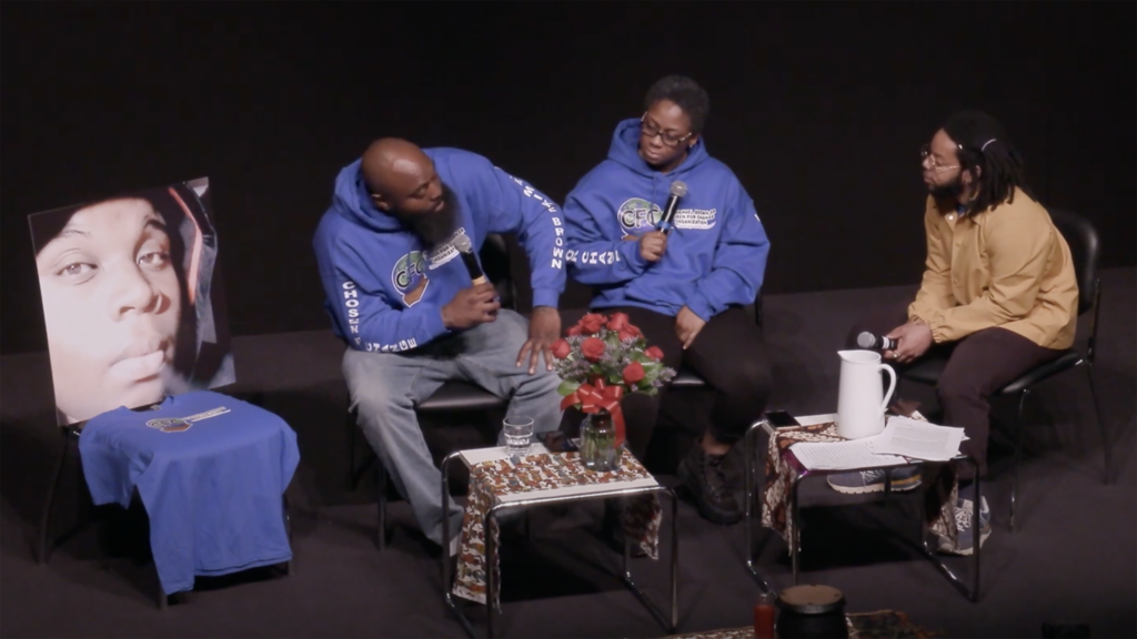 Michael Brown's father and stepmother talk with Rashad Timmons on stage about keeping their son's memory alive. A large photo of Michael Brown's face sits on a chair beside his father.