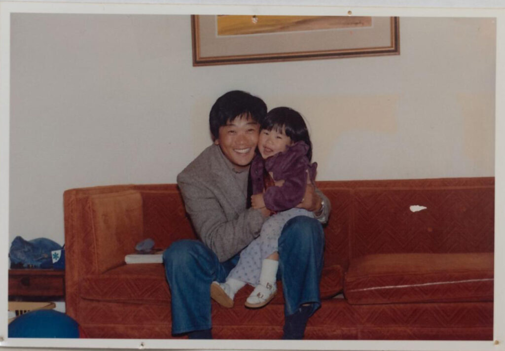 A man wearing a jacket and jeans sitting on a red couch with a young girl on his knee