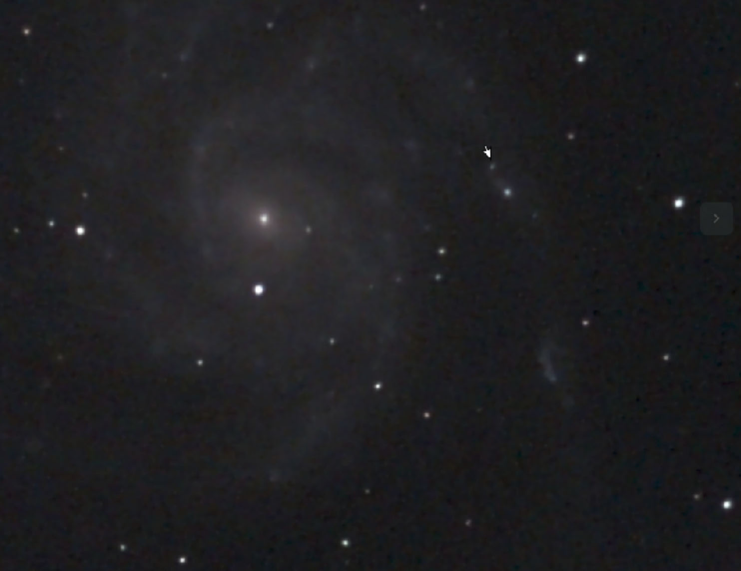 A photo of outerspace, black with a vague white swirl on the top right that covers most of the image. There are white little dots spread throughout.