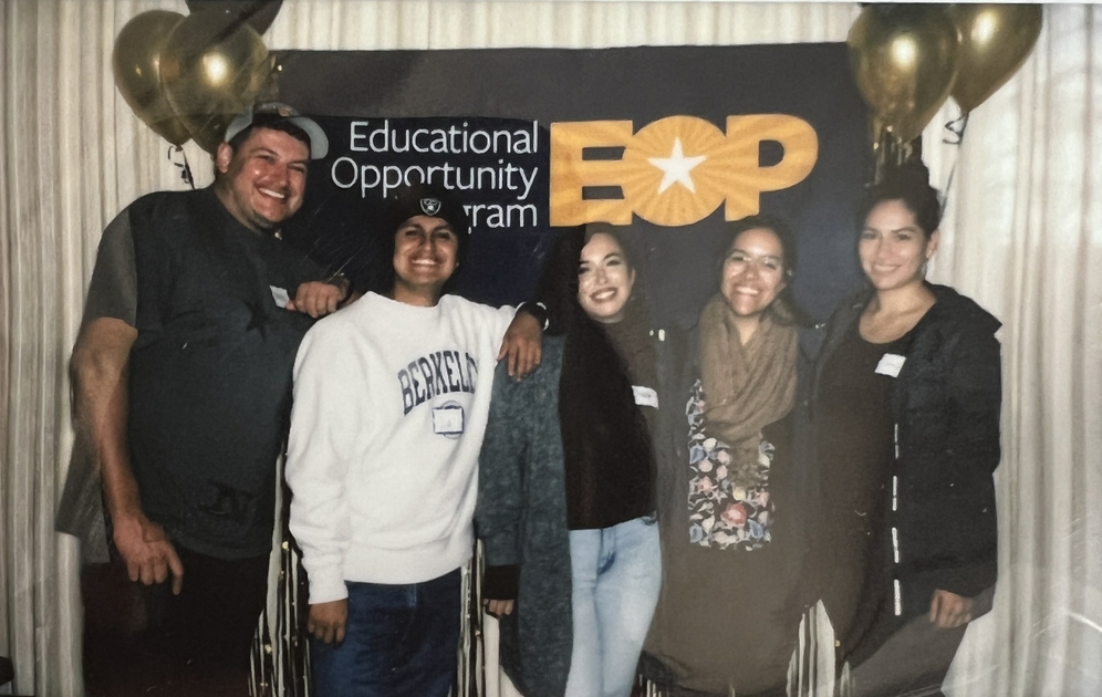 Luis posing with four other individuals in a line, smiling, in front of a sign that reads "Educational Opportunity Program EOP"