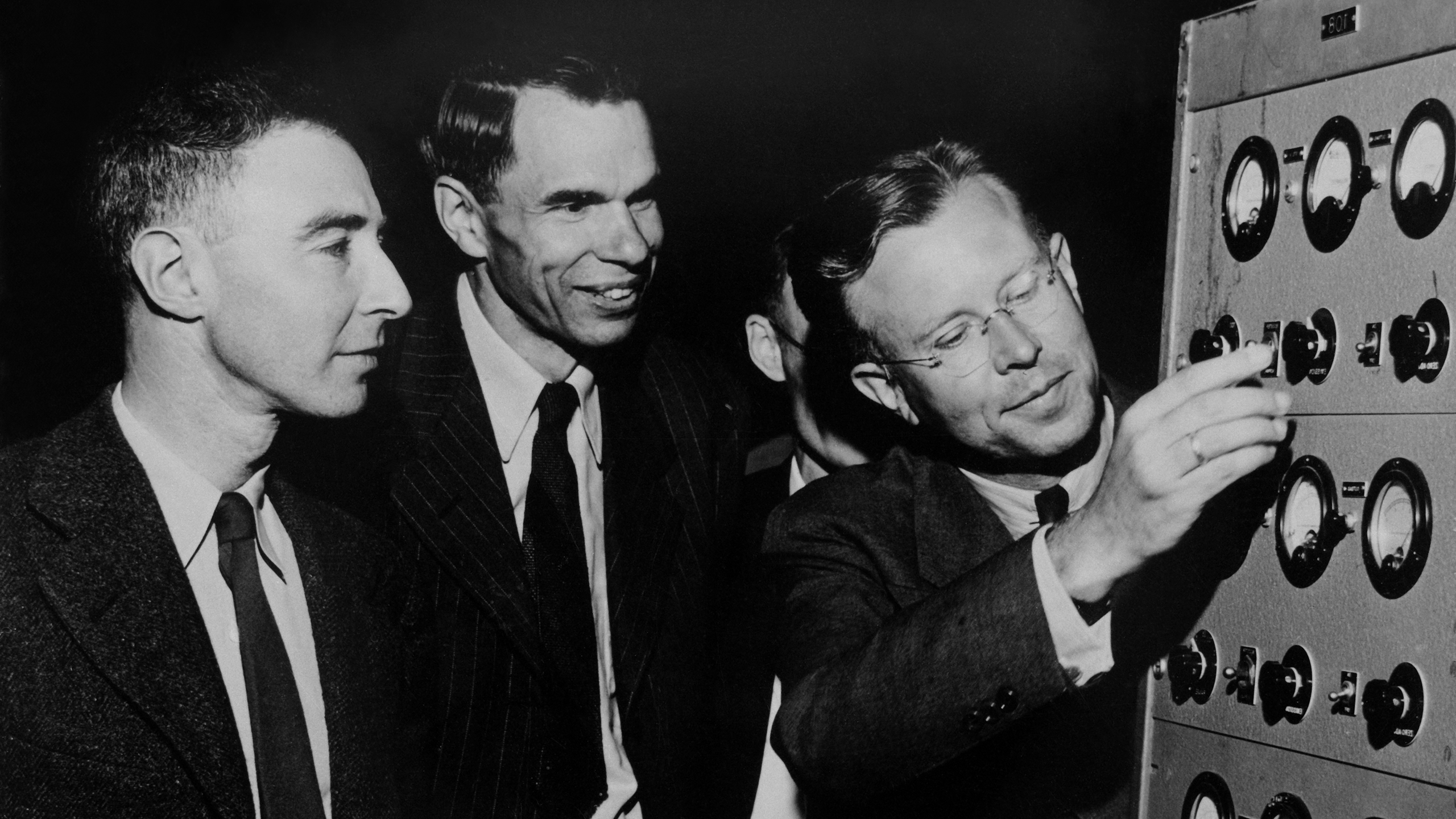Black-and-white photo of J. Robert Oppenheimer, Glenn T. Seaborg and Ernest O. Lawrence standing next to each other in early 1946 at the controls to the magnet of the 184-inch cyclotron