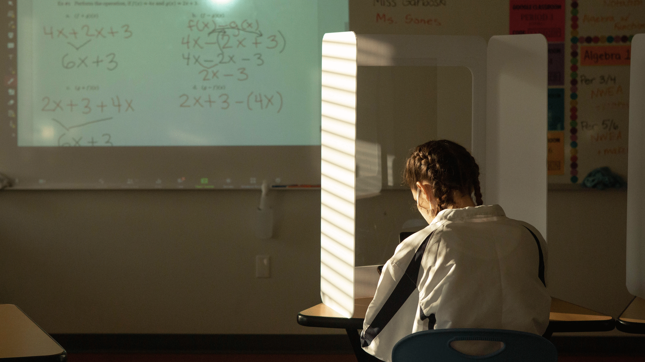 A young woman student in a darkened math class, looking through a protective screen at the calculations on a whiteboard