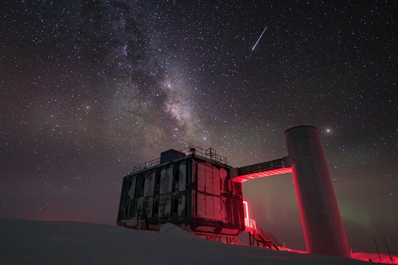 snowy scene of box-like building backlit in red against the starry sky