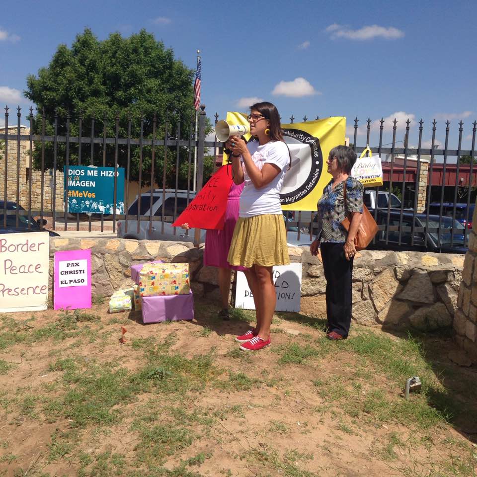 The campus's new tribal liaison, Tedde Simon, in 2016 in El Paso, Texas, where she is using a megaphone to speak at a rally at an immigration detention facility. She is standing next to a wrought iron fence where there are posters with protest slogans in English and Spanish.