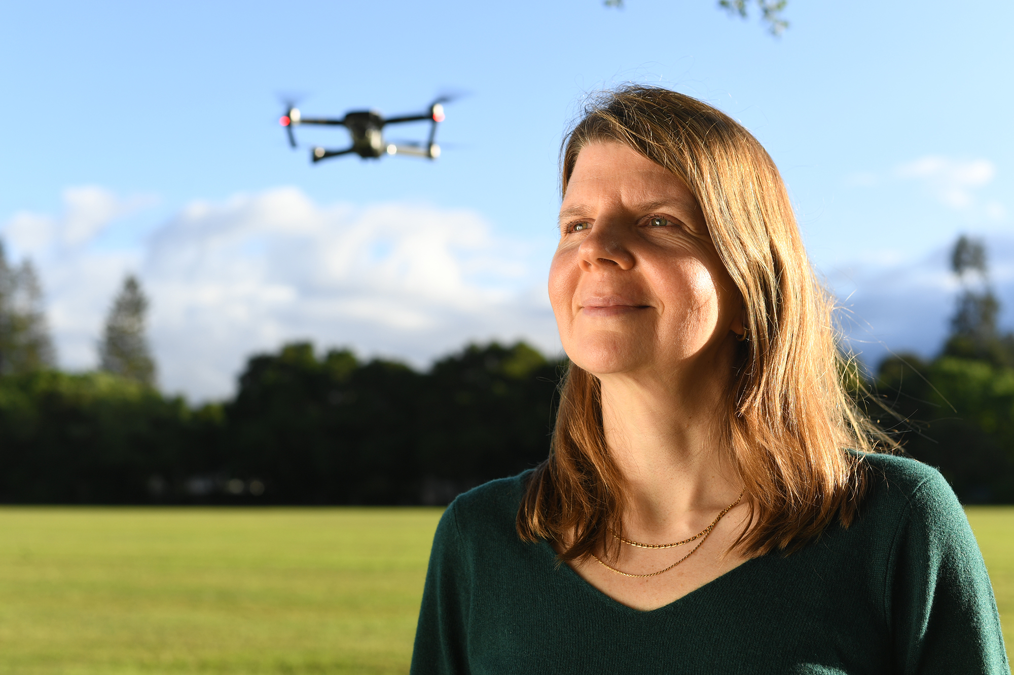 woman in green sweater looking to side with drone in air in background