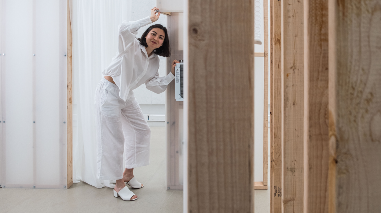 A portrait of Liz Gálvez, smiling, in an under-construction room of white plastic walls and wooden beams