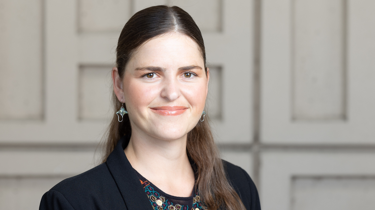 A headshot of Alejandra Echeverri, smiling, against a beige, cubic wall