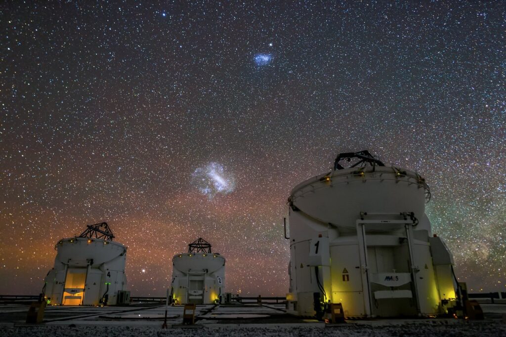 2 telescopes on a dark night with stars and two bright galaxies in the sky