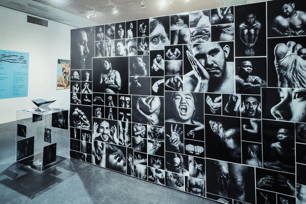 A wall of black-and-white photos of men in various poses that connote vulnerability