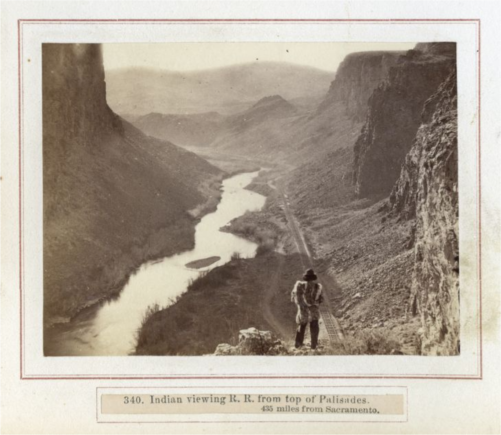 black-and-white photo of a Native American standing on a mountain overlooking the transcontinental railroad and a waterway