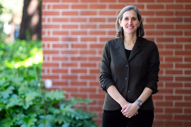 Amy Lerman standing in front of a red brick wall, with a mass of green plants at the left