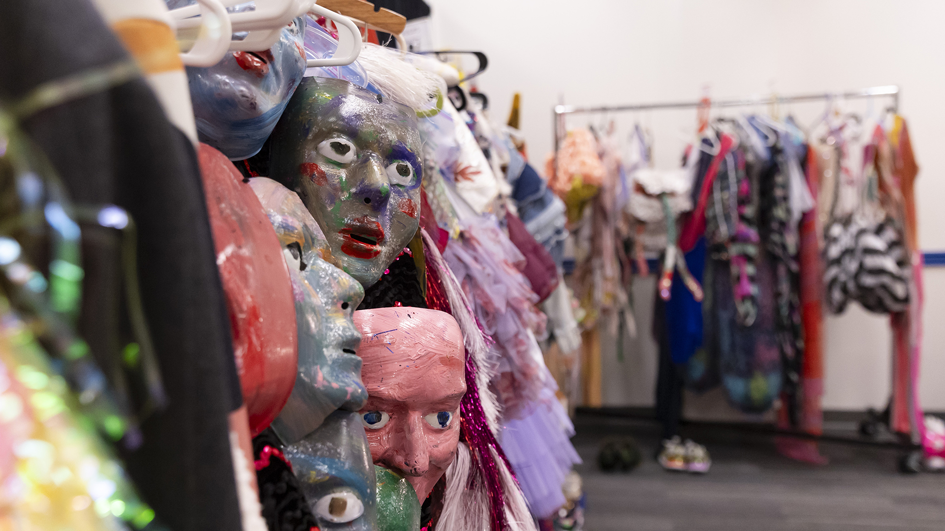 Costumes and masks hang from racks in a dressing room