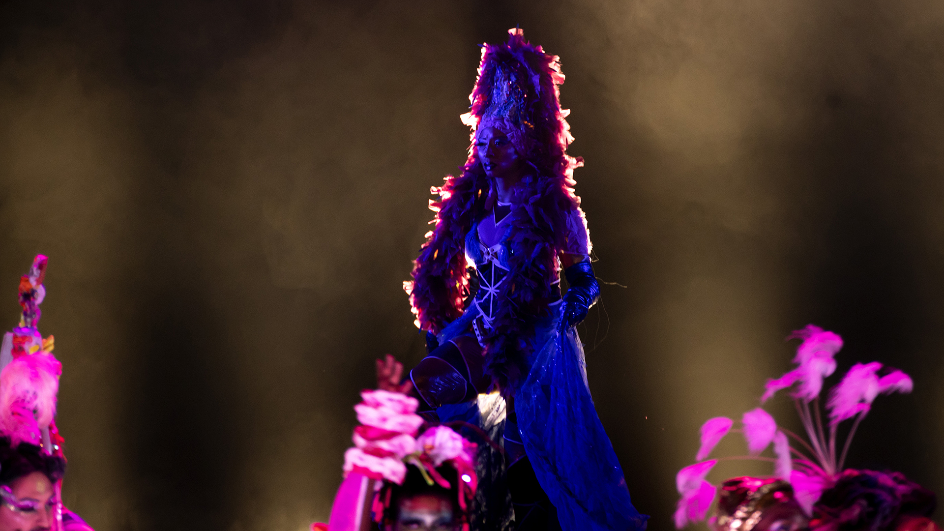 a silhouette of a person in a long dress and tall headwear, with a purplish hue around her ringed by a reddish-orange light that looks like fire, performs on stage