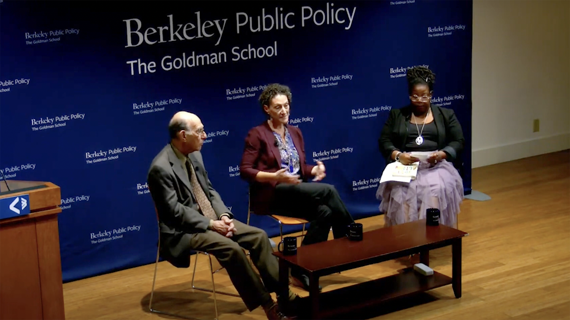 Richard Rothstein and his daughter, Leah Rothstein, and Tamika Moss, sit on stage while giving a talk for an audience
