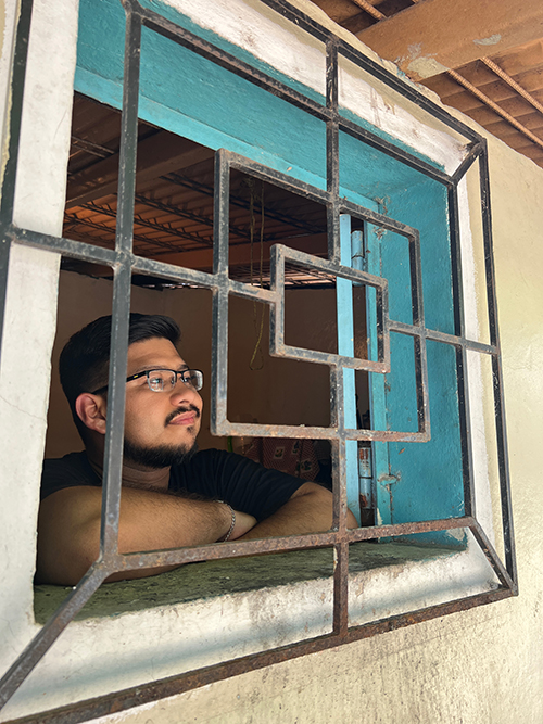 A young Salvadoran man with a thoughtful expression on his face looks out of a window fortified by bars