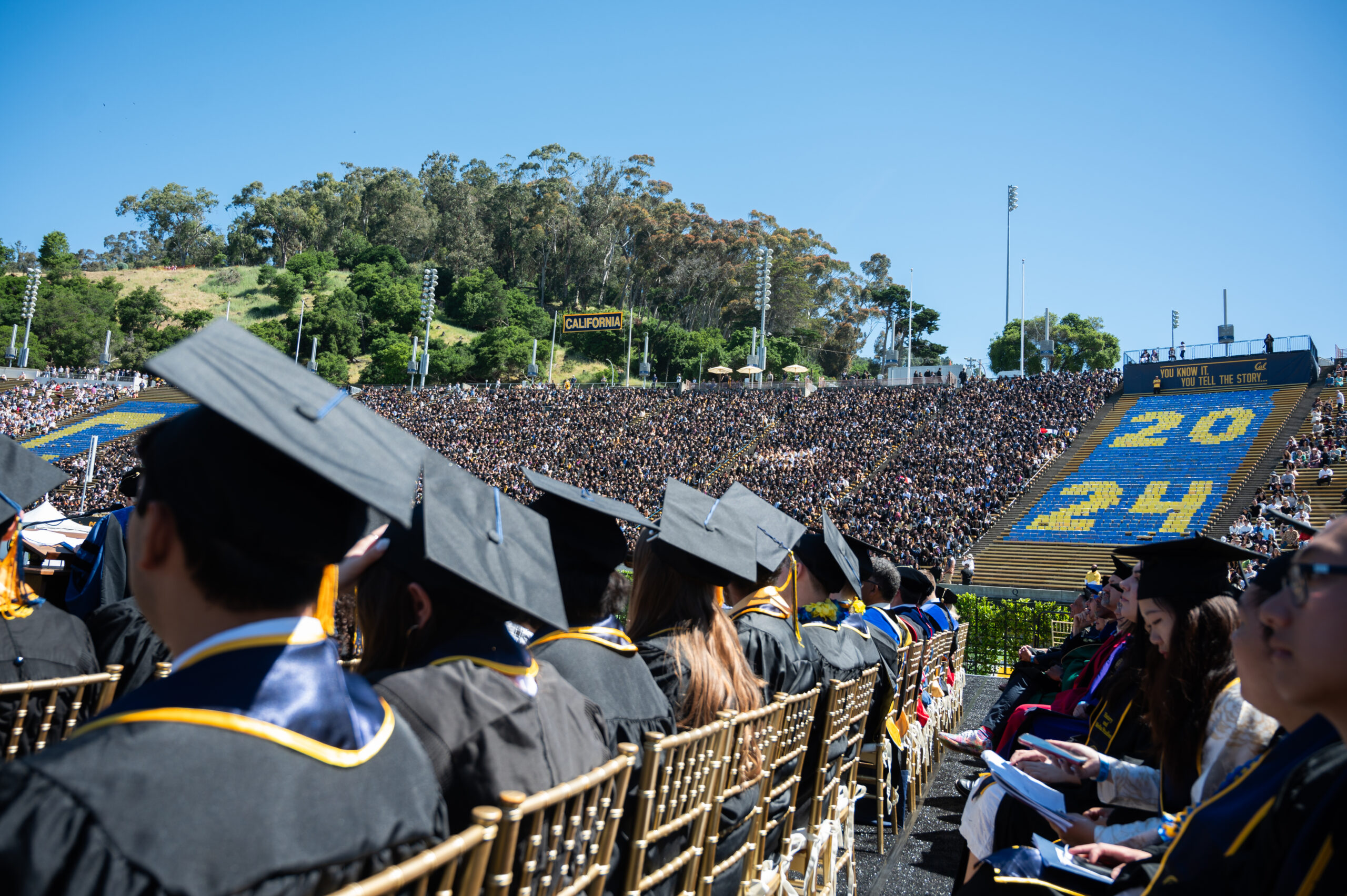 Students wearing graduation regalia sit, listening to speakers at UC Berkeley's spring commencement