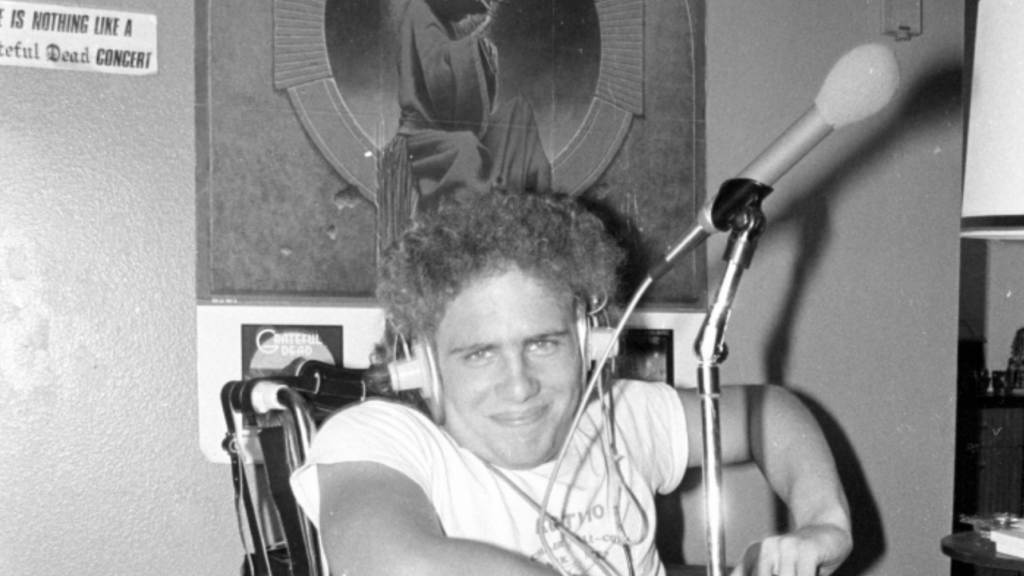 Black-and-white photo of Jim in his 20s in a sound studio with headphones on and a mic nearby