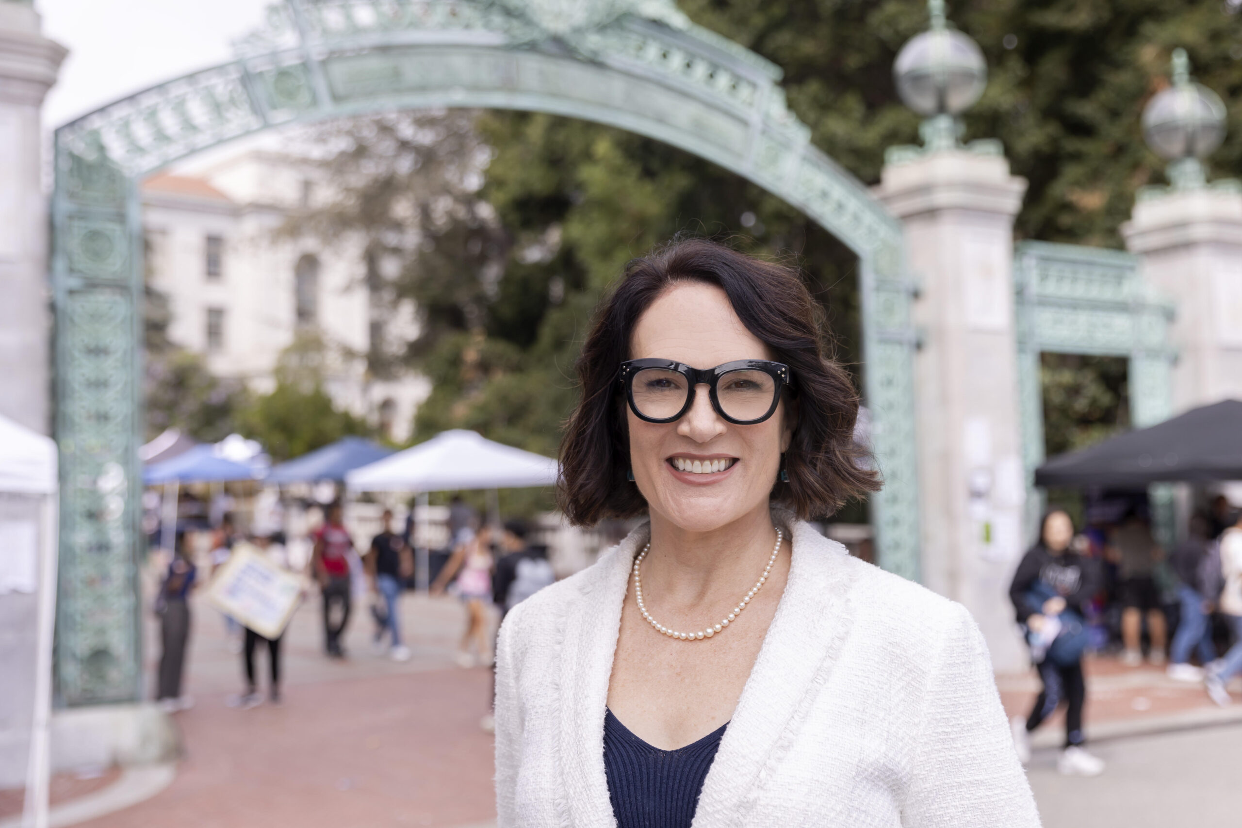Wendy Hillis wearing black glasses and a white suit stands in front of Sather gate.