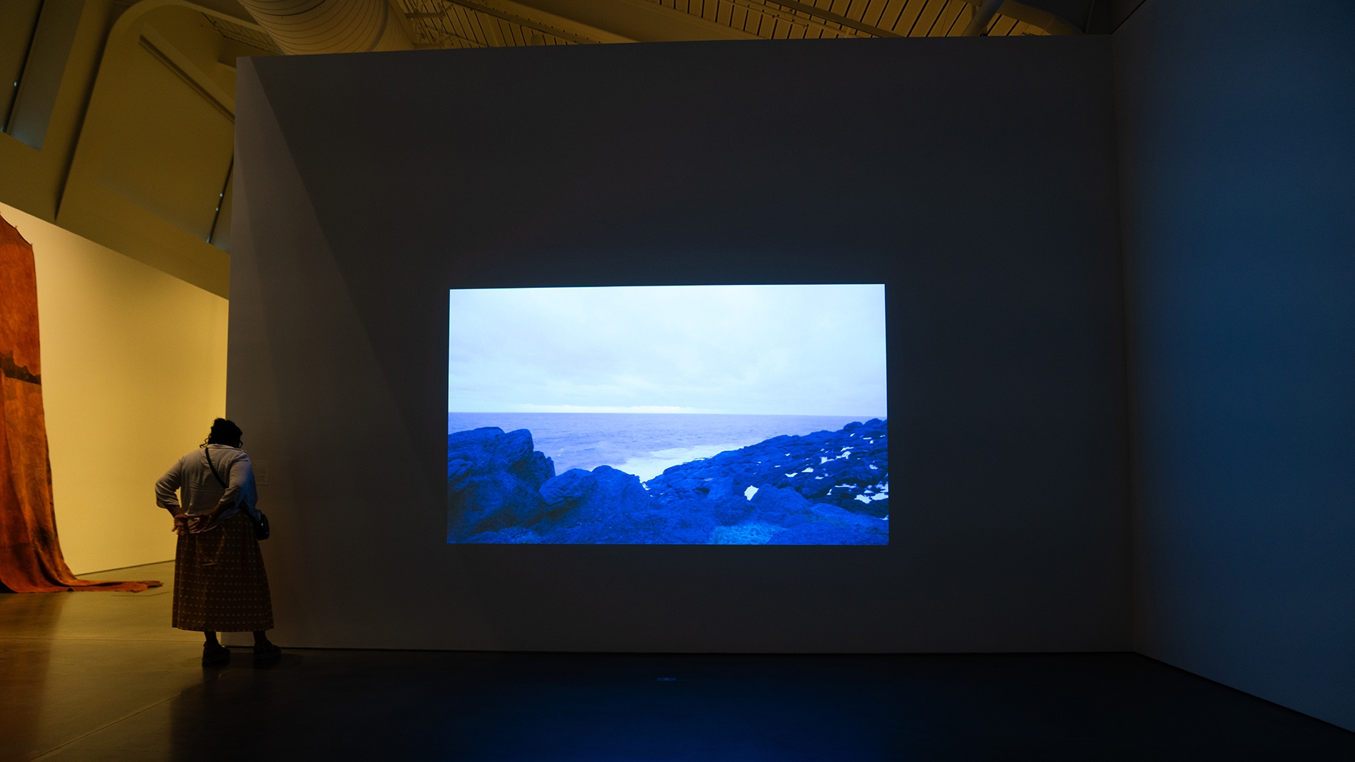 a person stands in a dark art gallery room next to a film projection on the wall