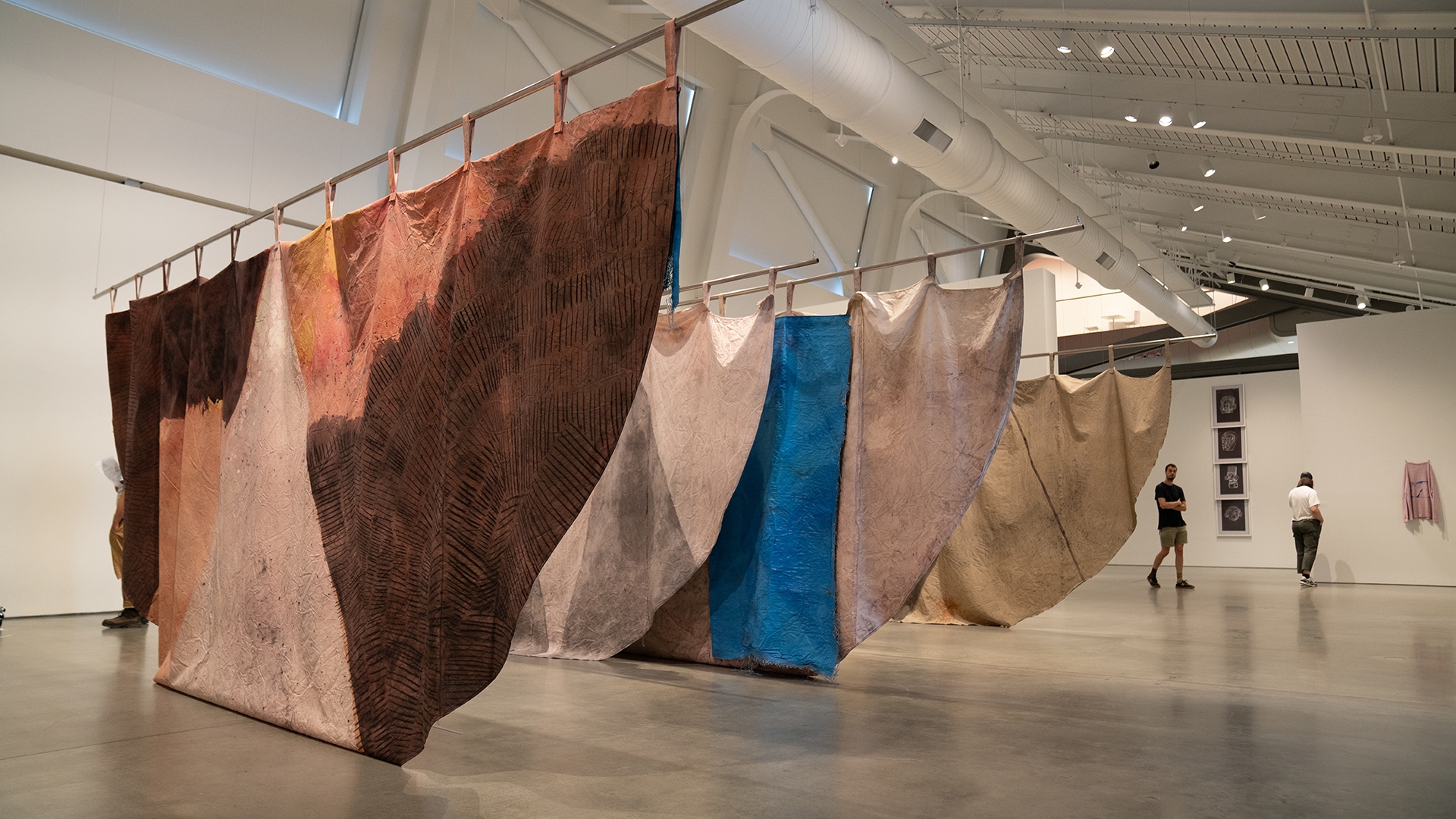 Giant canvas and linen artworks dyed with colorful natural dyes hang from polls in an art gallery