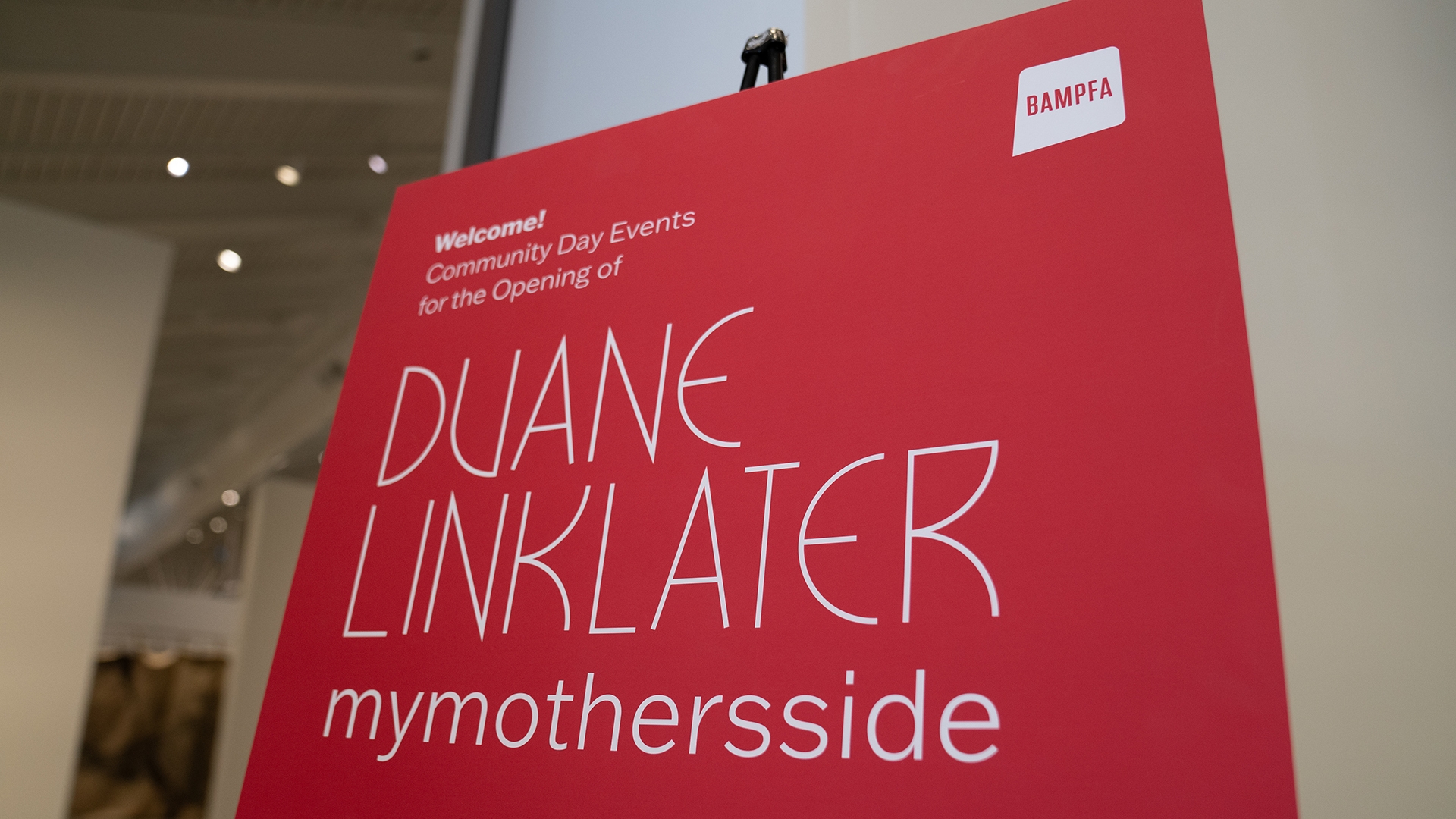 a red sign welcoming guests to an art exhibition by Duane Linklater
