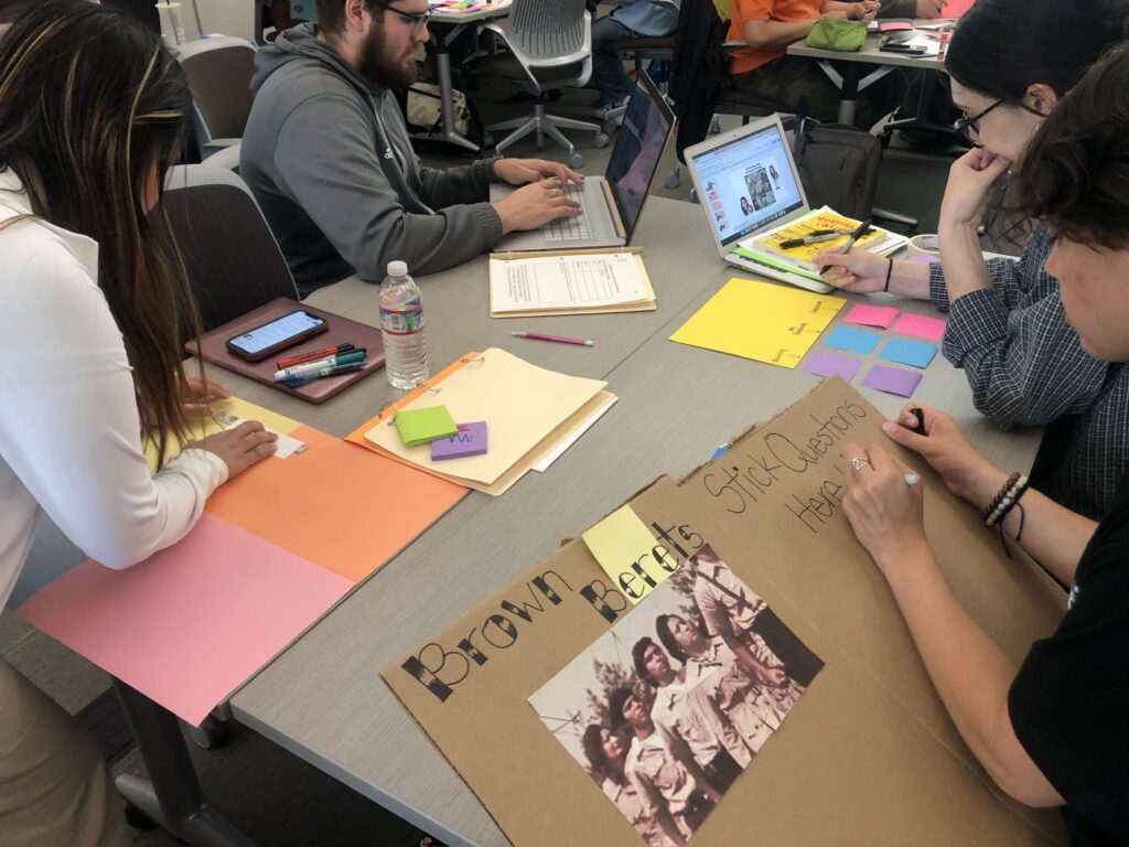 Students in Salahuddin's class sit at a table with laptops and poster board.