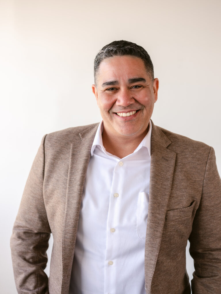 Jason Muñiz wearing a beige suit and smiling.