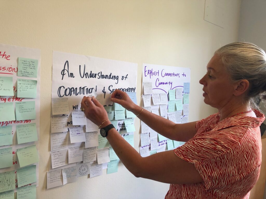Victoria Robinson placing a post-it note on a poster board on the wall during a workshop.