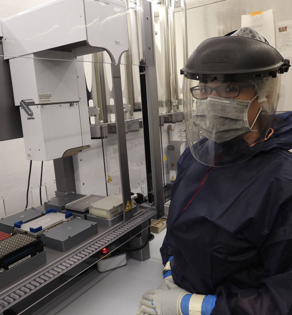 woman in mask, gown and gloves in from of a machine