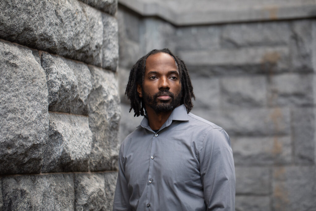 Elijah Baucom, an instructor in Citizen Clinic, UC Berkeley's cybersecurity clinic, which is a semester-long course, looks out into the distance with a serious look on his face as he stands next to a stone wall on campus. 