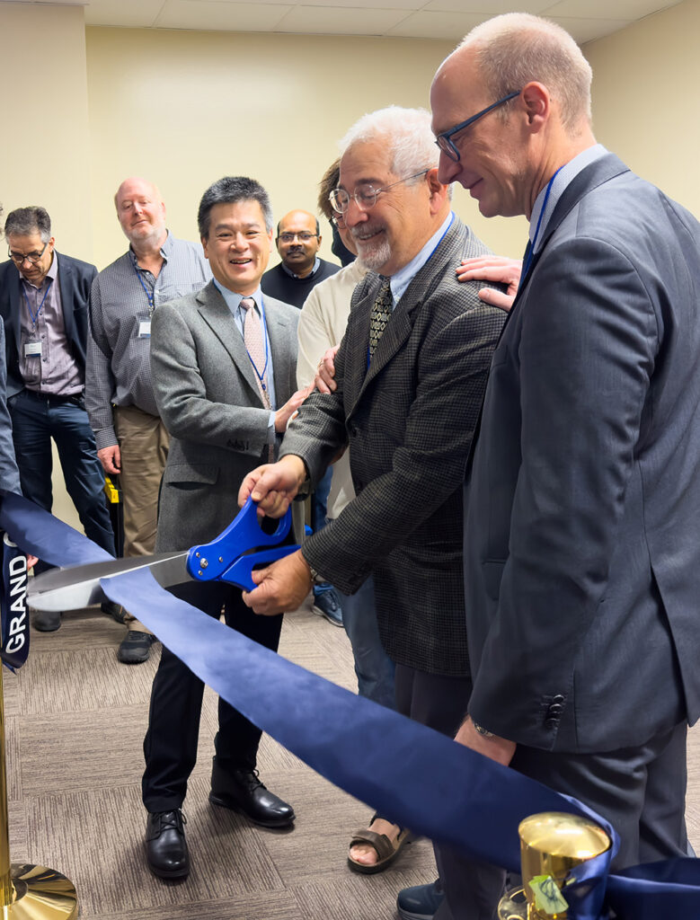 three men in suits using large scissors to cut blue ribbon